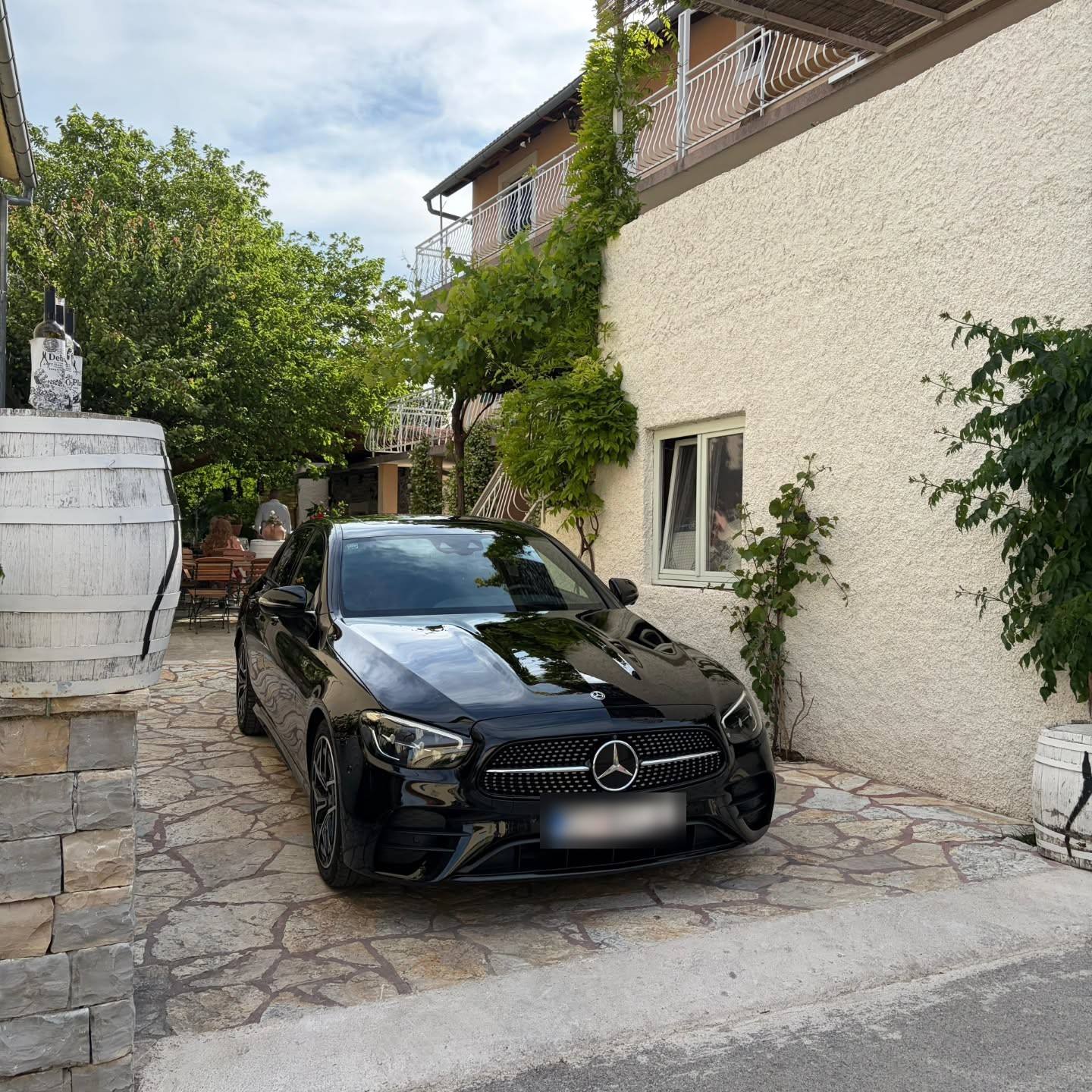 Crni automobil na kamenom popločenju uz kuću obraslu lozom